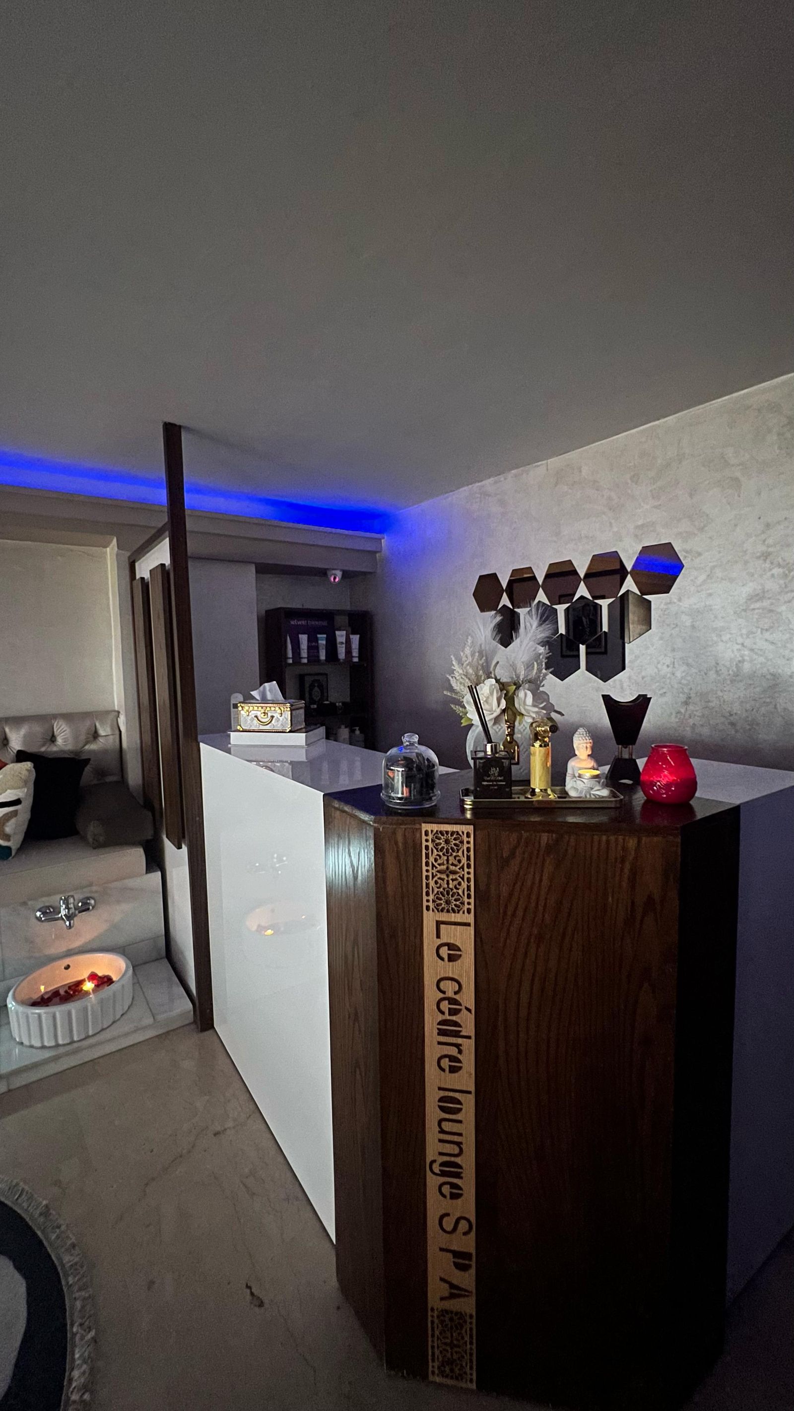 Comptoir d’accueil en bois gravé « Le Cèdre Lounge SPA » avec bougie, statuette et bain de pieds fleuri