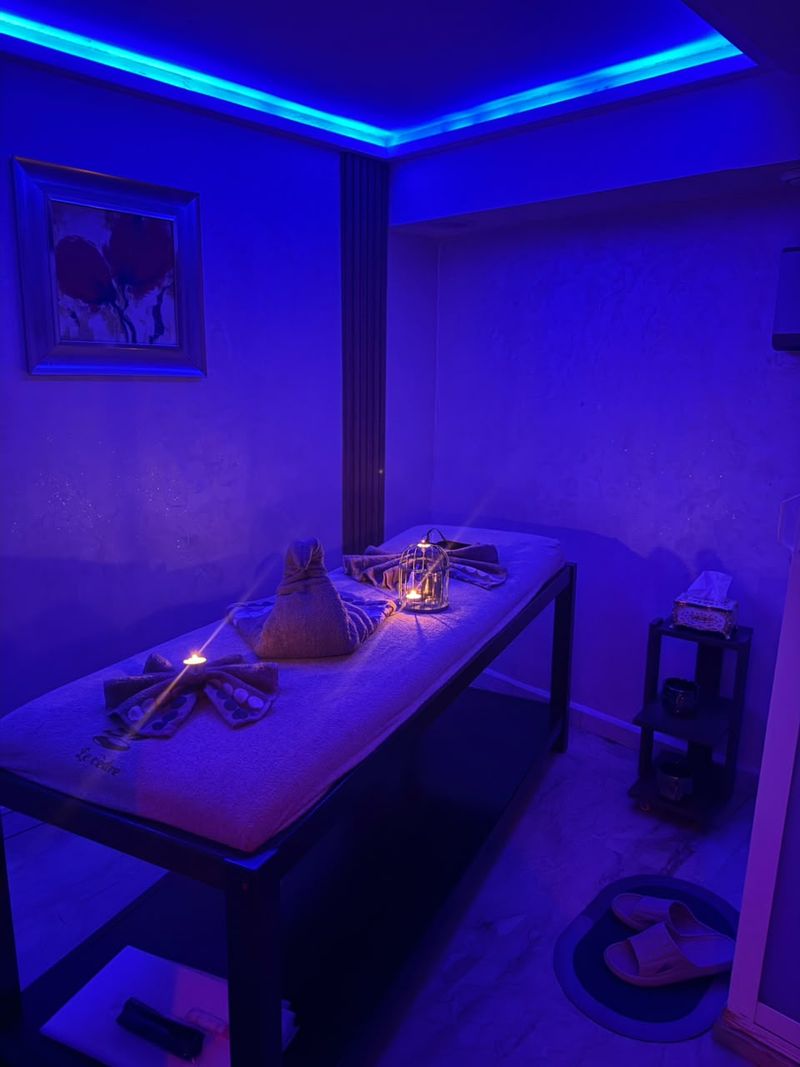 Cabine de massage sous lumière bleue avec serviettes nouées, bougie et lanterne dorée
