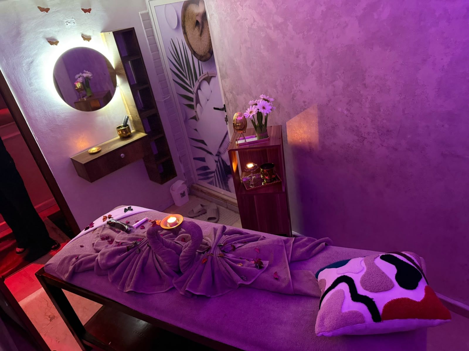 Vue plongeante d’une cabine de massage de Le Cèdre Lounge Spa sous lumière violette, serviettes pliées en cygne et coussin brodé