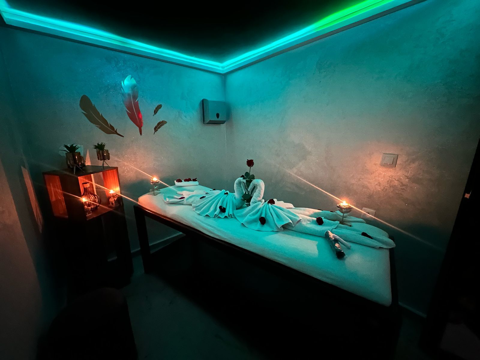 Cabine de soin de Le Cèdre Lounge Spa à Casablanca : table de massage habillée de serviettes blanches, roses et bougies, sous une lumière turquoise