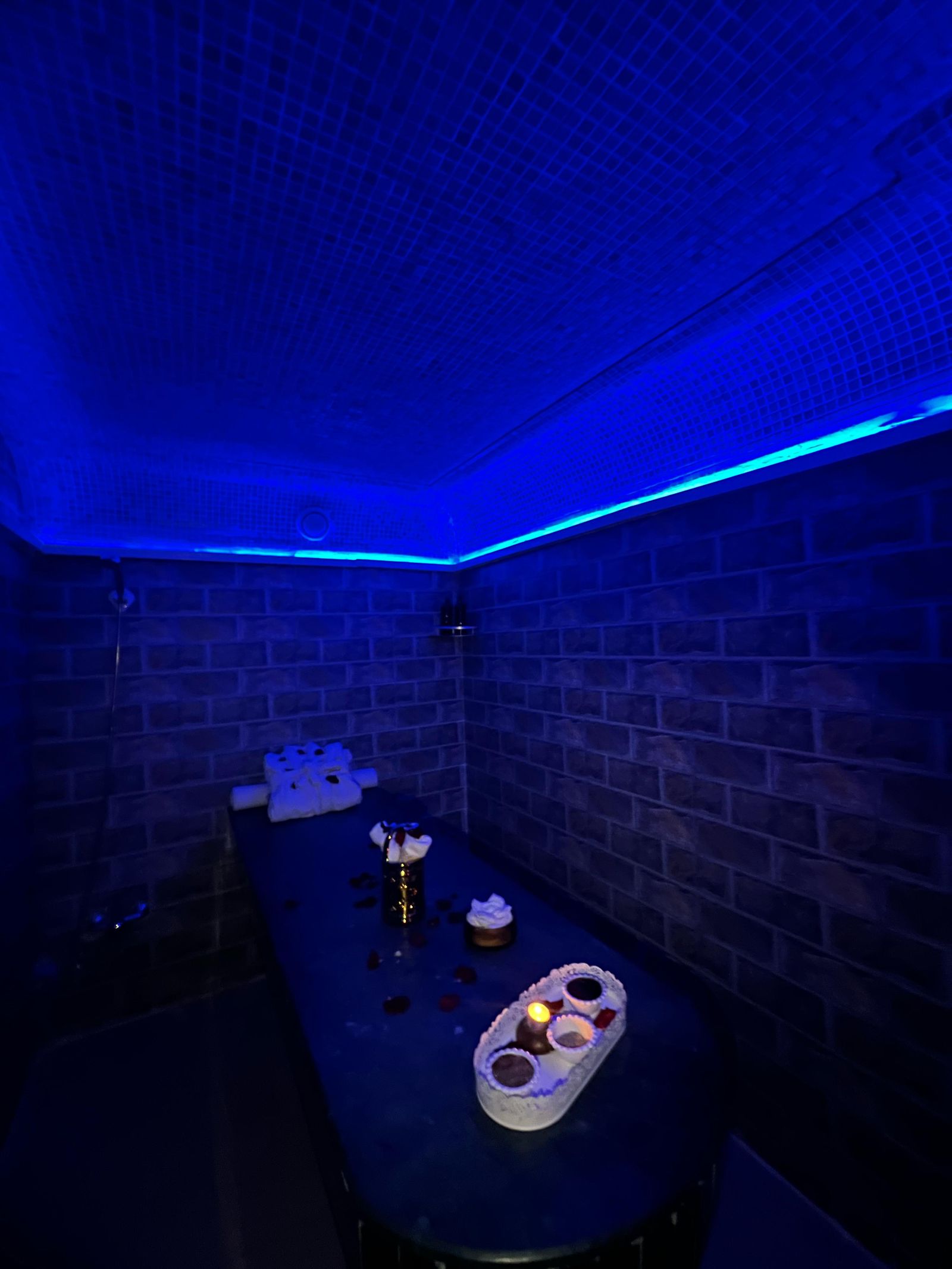 Hammam traditionnel de Le Cèdre Lounge Spa à Casablanca, banc en marbre, serviettes roulées et bougies sous une lumière bleue