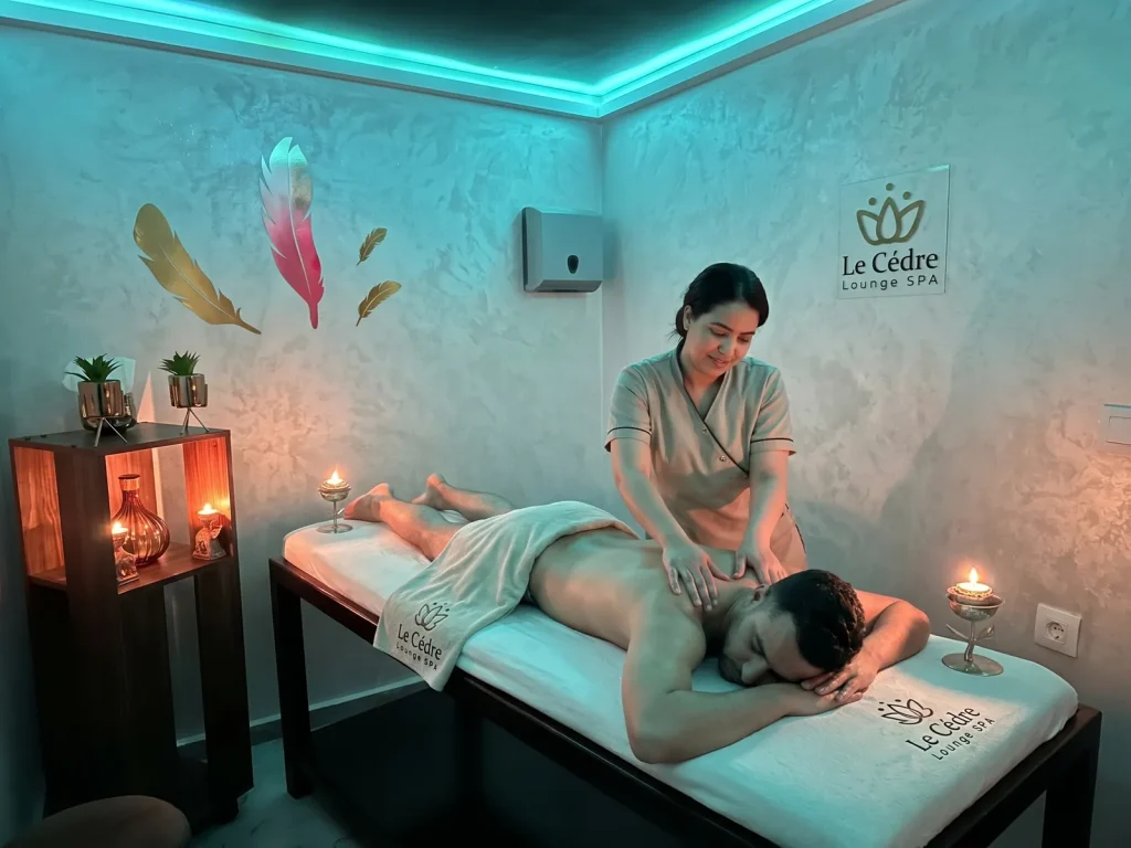 تدليك مريح للظهر في مقصورة خاصة في Le Cèdre Lounge Spa بالدار البيضاء، سقف بإضاءة فيروزية وريش زخرفي على الجدار وشموع